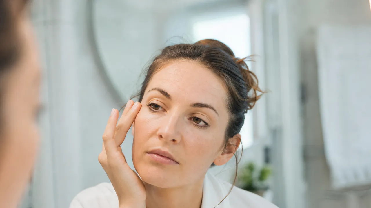 Femme touchant doucement le coin de son œil devant le miroir d'une salle de bain